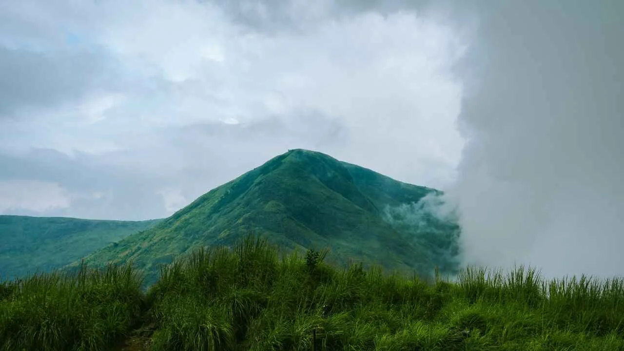 a green mountain with clouds