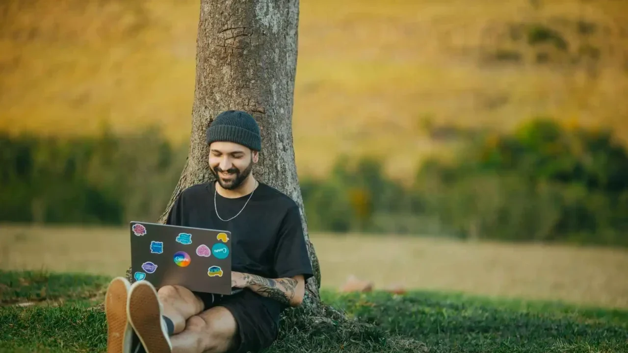 a man sitting next to a tree with a laptop